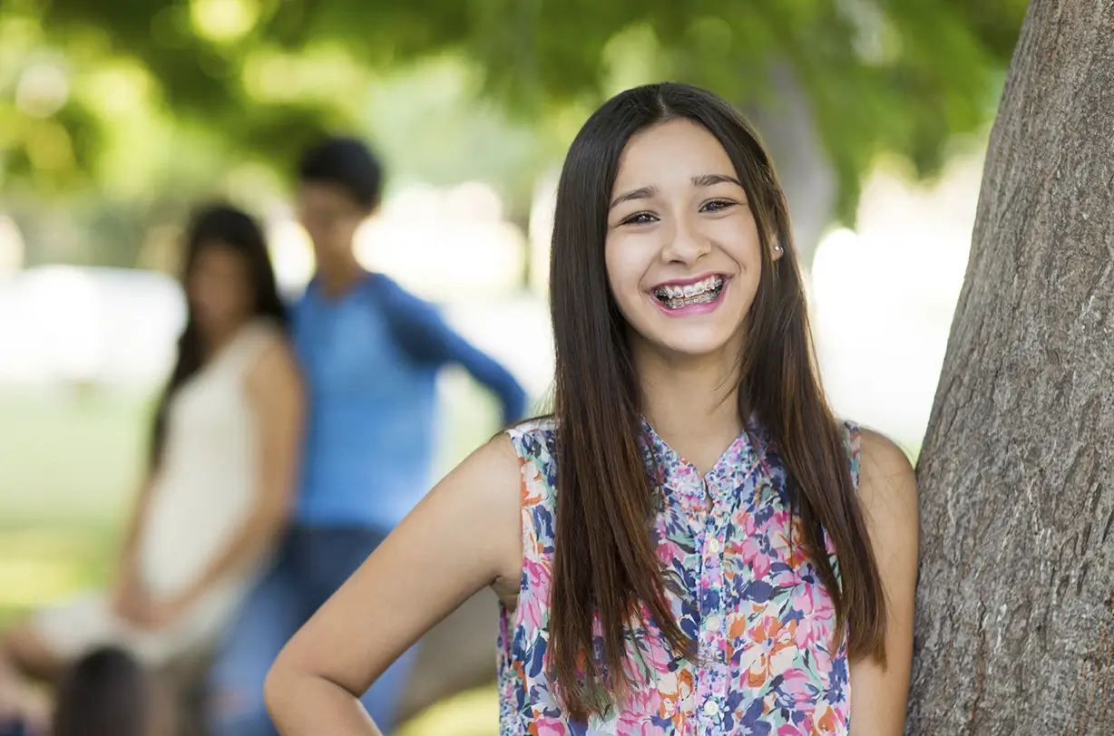 Girl with braces smiling next to tree