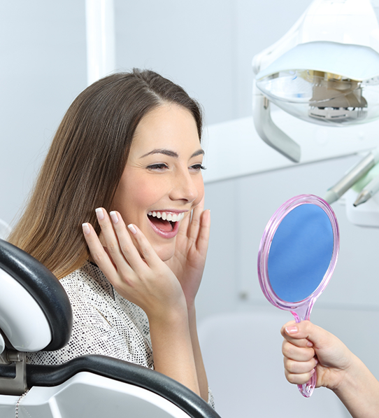 Woman in dental chair smiling at handheld mirror