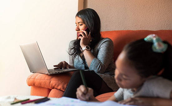 Woman on couch working on laptop and talking on phone