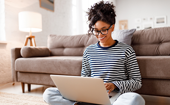 Woman sitting in front of couch typing on laptop