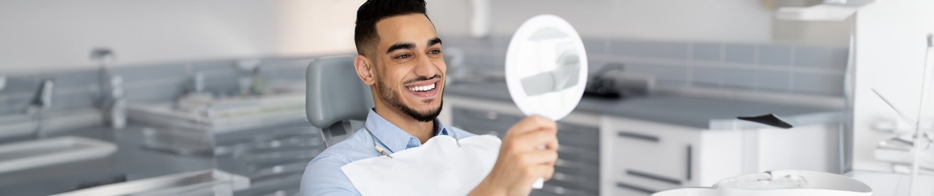 Man in dental chair checking smile in handheld mirror