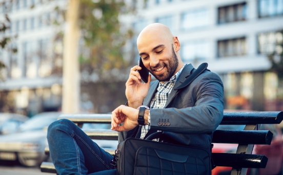 Man on bench checking watch and talking on phone