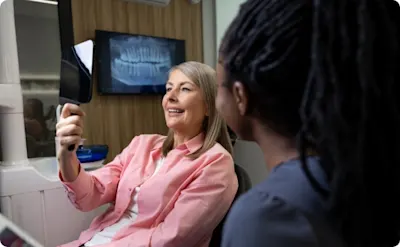 Female patient holding up mirror to look at teeth