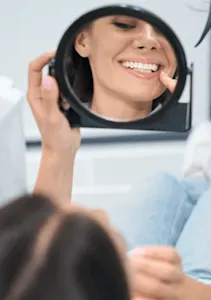 Female dental patient checking teeth in handheld mirror