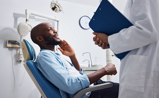 Male dental patient touching jaw and smiling up at dentist