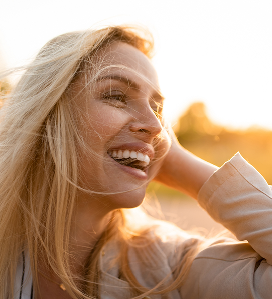 Woman with blonde hair smiling outside in sun