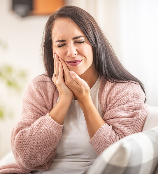 Woman sitting on couch rubbing tooth in pain