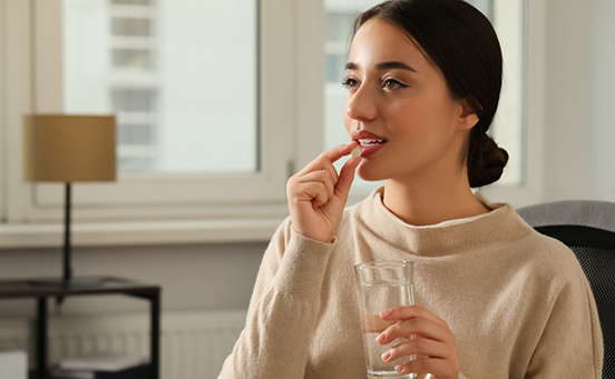 Woman holding glass of water and taking pill